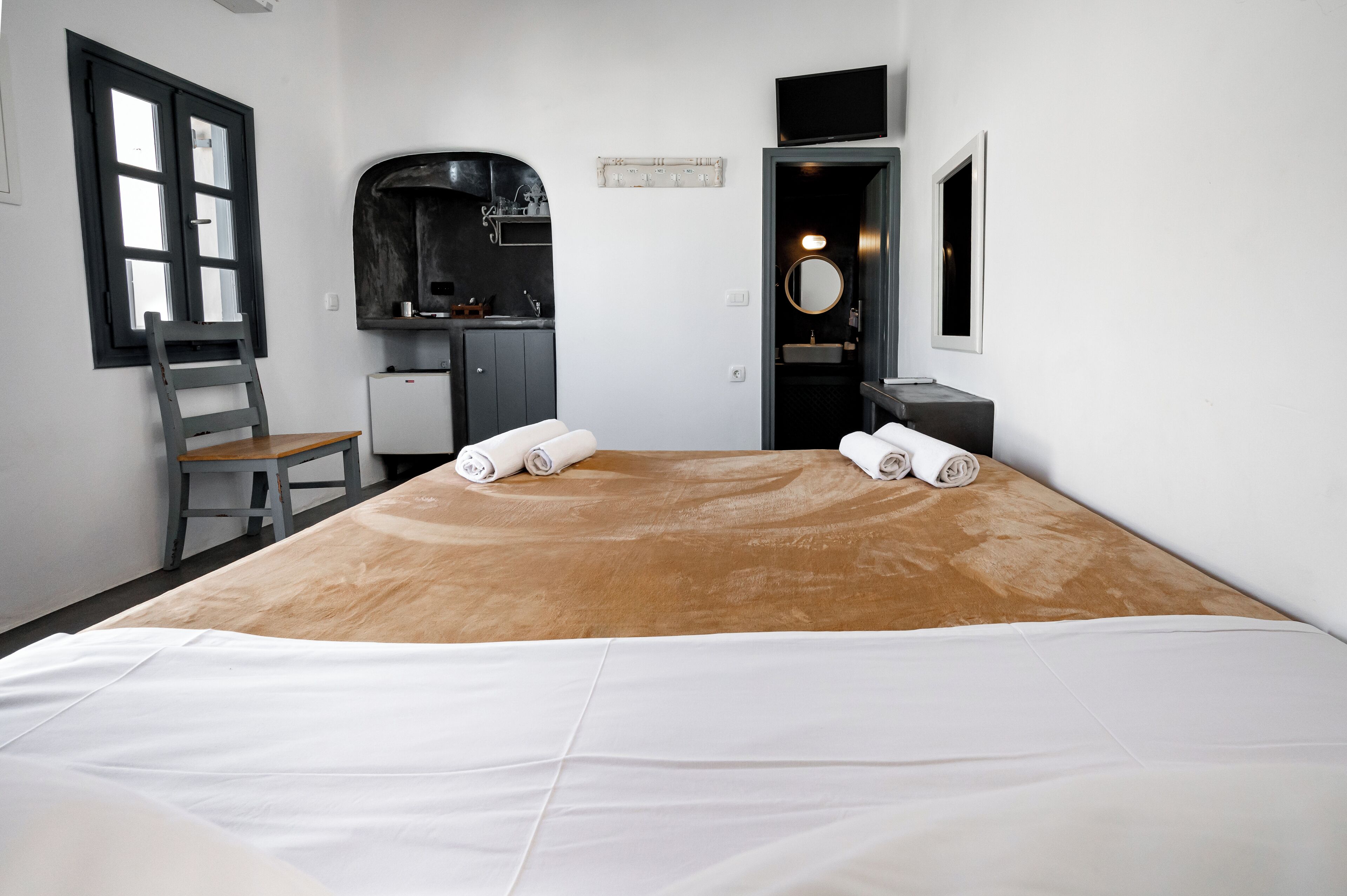Une chambre d’hôtel avec un grand lit, un bureau avec une chaise, une petite kitchenette, un miroir et un téléviseur.