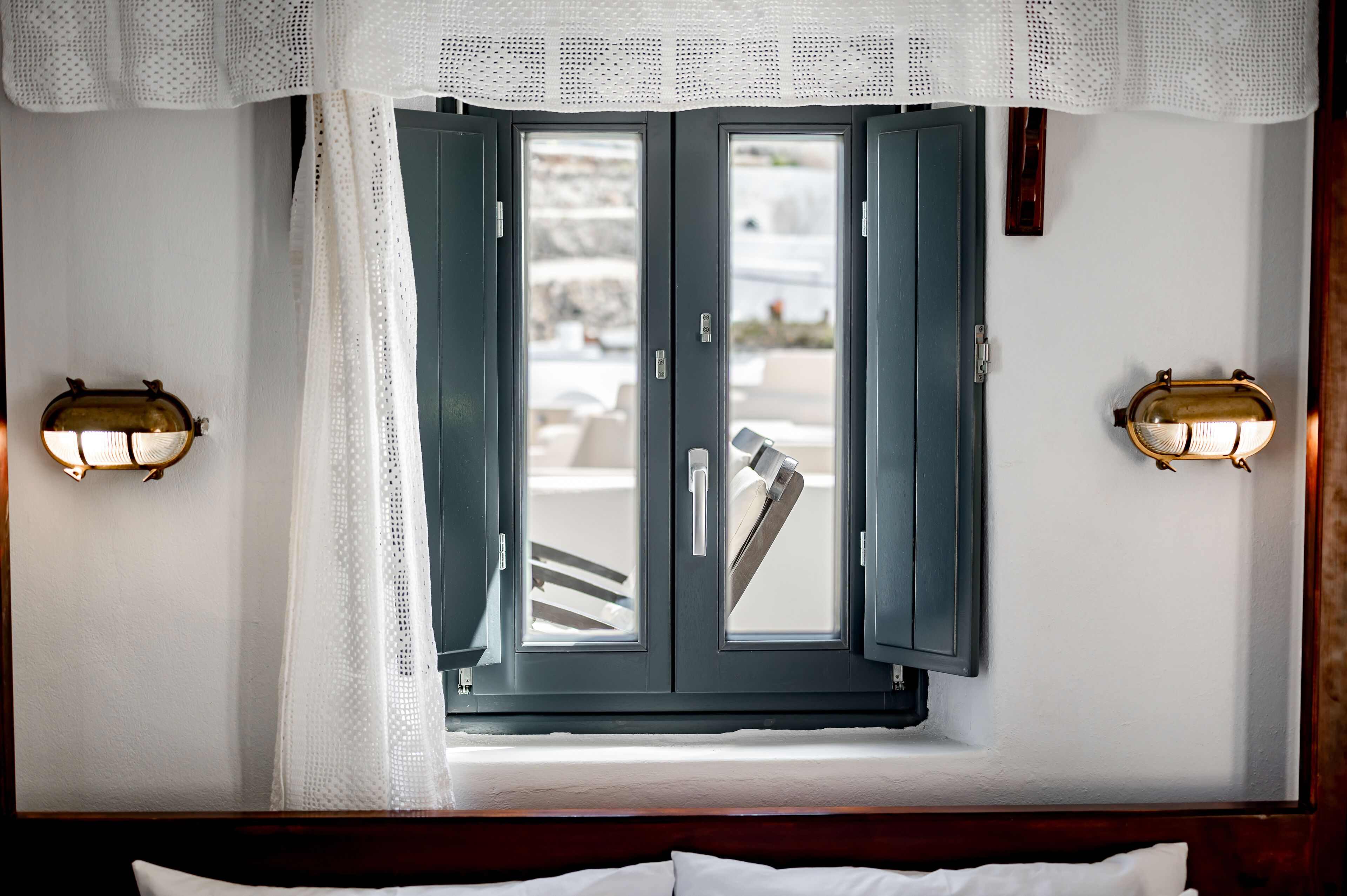 A room with a bed, a window with curtains, and two wall-mounted light fixtures.