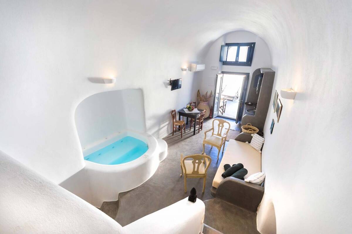 A compact, white-walled room with a bathtub, a dining area, and a small kitchen.
