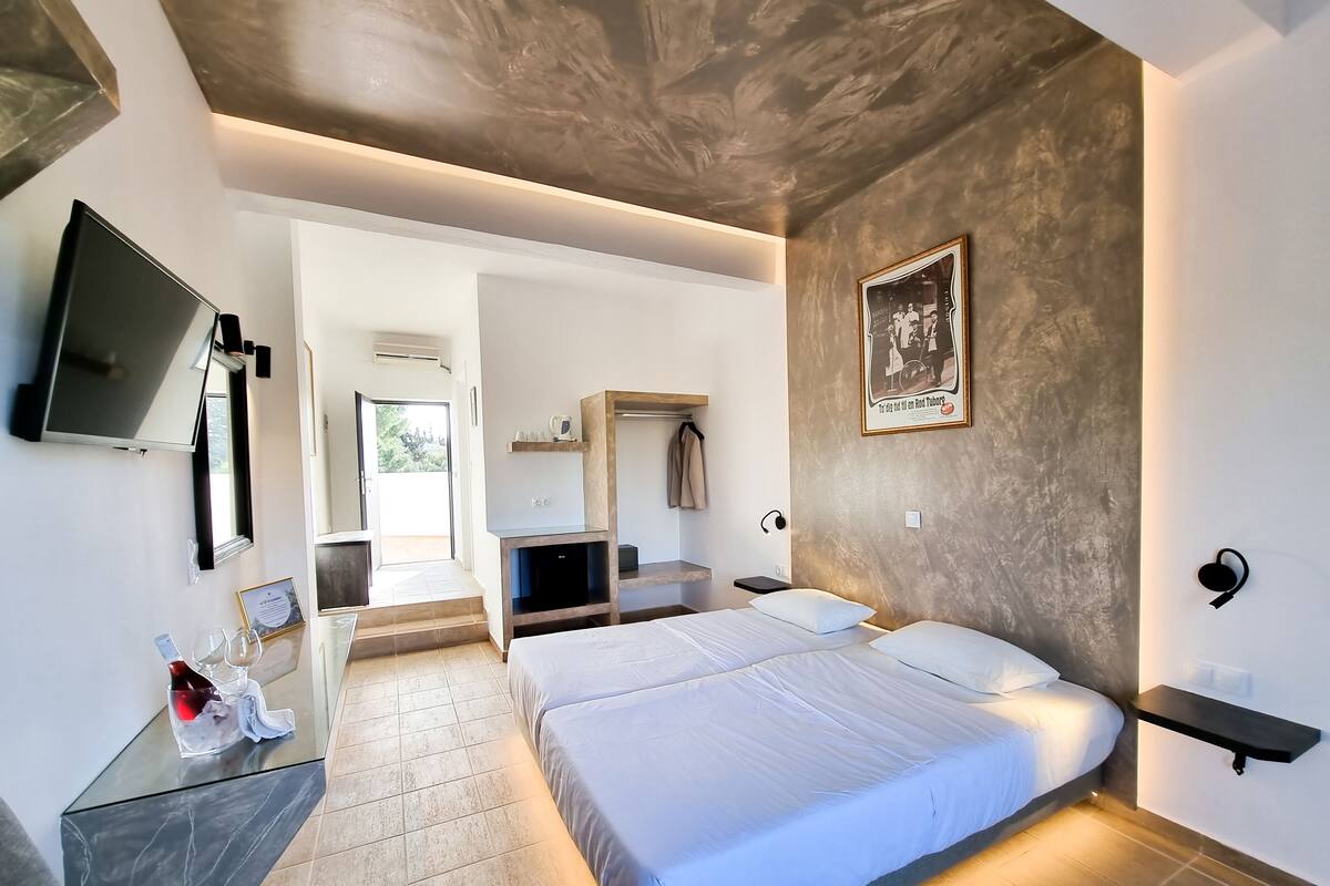 Ein modernes Hotelzimmer mit einem großen Bett, Nachttischen, einem Flachbildfernseher und einer Tür zu einem Balkon.