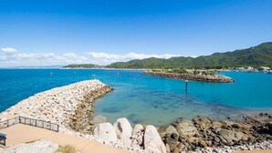 A coastal view with a rocky breakwater, clear blue water, and distant hills. - 1 Bright Point Apartment 3303 (Nelly Bay)