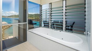A modern bathroom with a large bathtub, a glass-enclosed shower area, and a view of a coastal landscape. - 1 Bright Point Apartment 3303 (Nelly Bay)