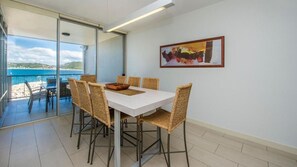 A dining area with a table and chairs, a view of the sea, and a painting on the wall. - 1 Bright Point Apartment 3303 (Nelly Bay)