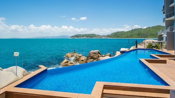 A swimming pool with a view of the sea, surrounded by rocks and a building. - 1 Bright Point Apartment 3303 (Nelly Bay)