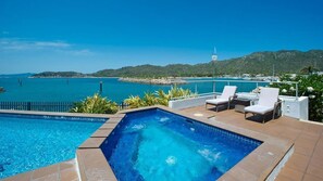 A swimming pool with a view of the sea and hills, outdoor seating, and a clear sky. - 1 Bright Point Apartment 3303 (Nelly Bay)
