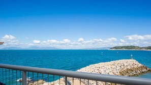 A coastal view with a rocky pier, clear blue sea, and distant land.