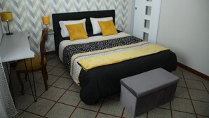 Una camera da letto ordinata con un letto, un comodino, una sedia e una piccola panca.