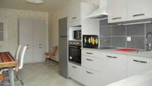 Una cucina moderna con mobili bianchi, un frigorifero in acciaio inossidabile, un forno e un lavello. Si nota un tavolo da pranzo con sedie e una sedia con cuscino rosso.