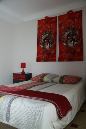 Une chambre à coucher avec un lit, une table de chevet et deux éléments de décoration rouge sur les murs.