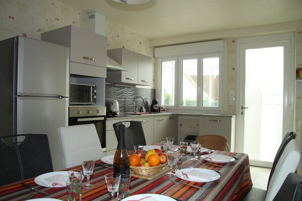 Une cuisine compacte dotée d’appareils électroménagers modernes, une table à manger pour quatre personnes et une vue sur l’extérieur grâce à une grande fenêtre.