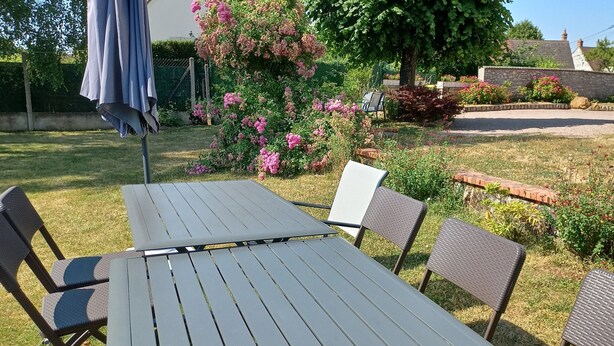 Un patio con tavolo e sedie, immerso in un giardino fiorito con piante e un albero.