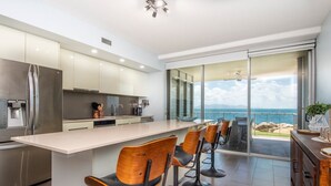 Une cuisine moderne dotée d’un grand îlot central, de tabourets de bar et offrant une vue sur l’océan.