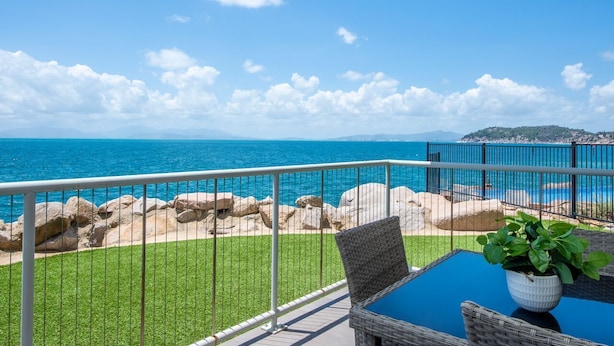 Un balcon avec vue sur la mer, une plante en pot et une chaise en osier.