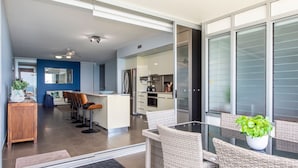 Une cuisine moderne équipée d’un réfrigérateur, d’une cuisinière et d’un coin repas avec des chaises en osier et une table en verre.
