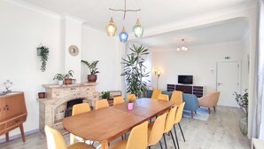 Zona pranzo moderna con camino in mattoni, sedie gialle e tavolo in legno. Sono presenti piante in vaso e un televisore su un mobile.