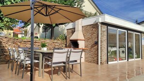 Patio esterno con muro in pietra, forno a mattoni e tavolo con sedie.