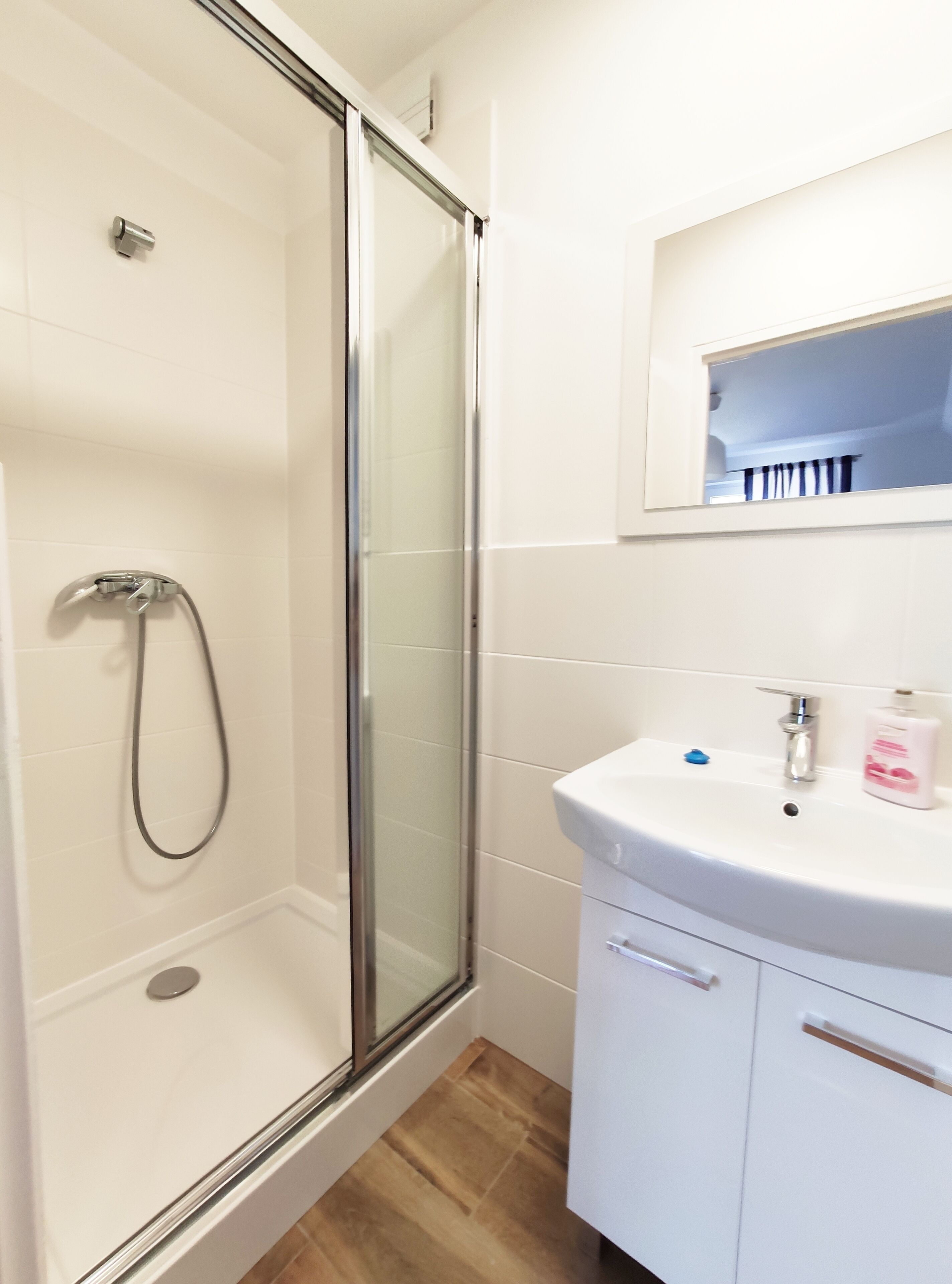 A bathroom with a glass-enclosed shower, a white sink with a mirror above it, and a small shelf with toiletries.