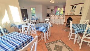 A dining area with multiple tables and chairs, a kitchen in the background, and a fireplace.