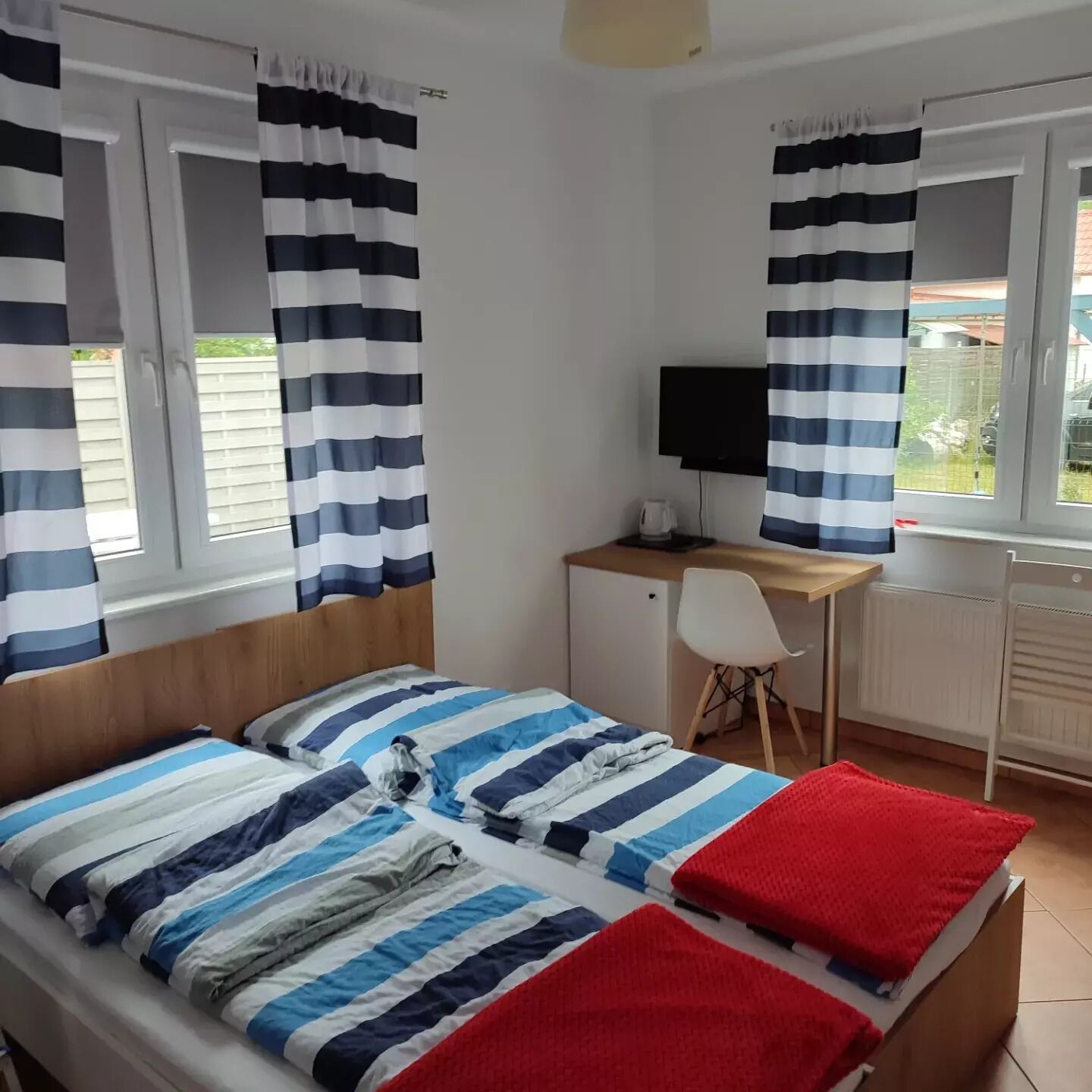 A bedroom with a bed, a desk, and a chair. There are curtains on the windows.