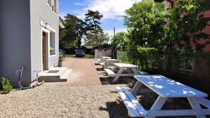 A gravel patio with picnic tables and a scooter, a building with a sign, and a clear blue sky.