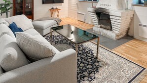 Ein Wohnzimmer mit Kamin aus Stein, einem Glastisch, einer Couch und einem gemusterten Teppich.