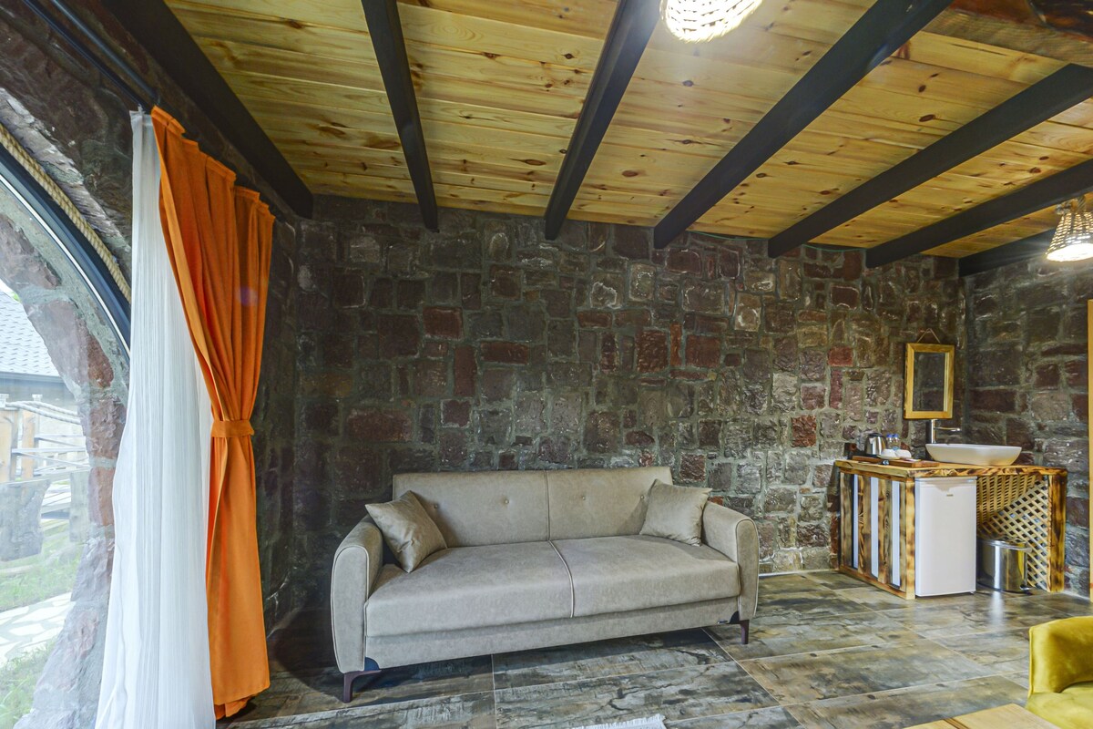 Ein Zimmer mit Steinwand, einer Couch, einer Holzbalkendecke und einem Fenster mit Vorhängen.