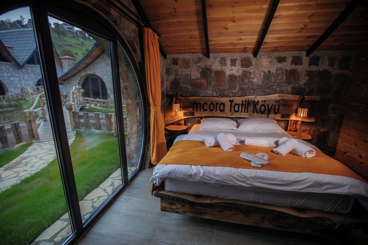A wooden room with a bed, a stone wall, and a view of a garden.