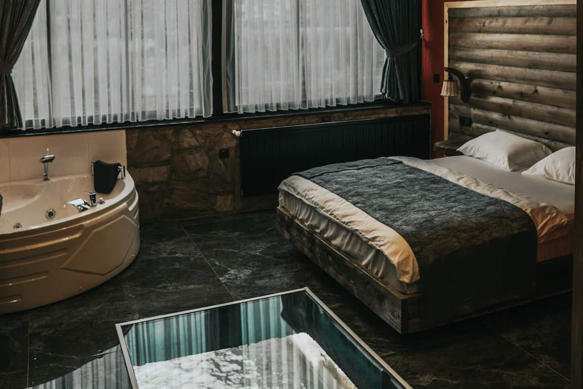A modern bedroom with a large bed, a separate bathtub, and a stone wall.