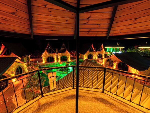 A balcony with a view of a stone building with multiple arches and a green-lit pathway.