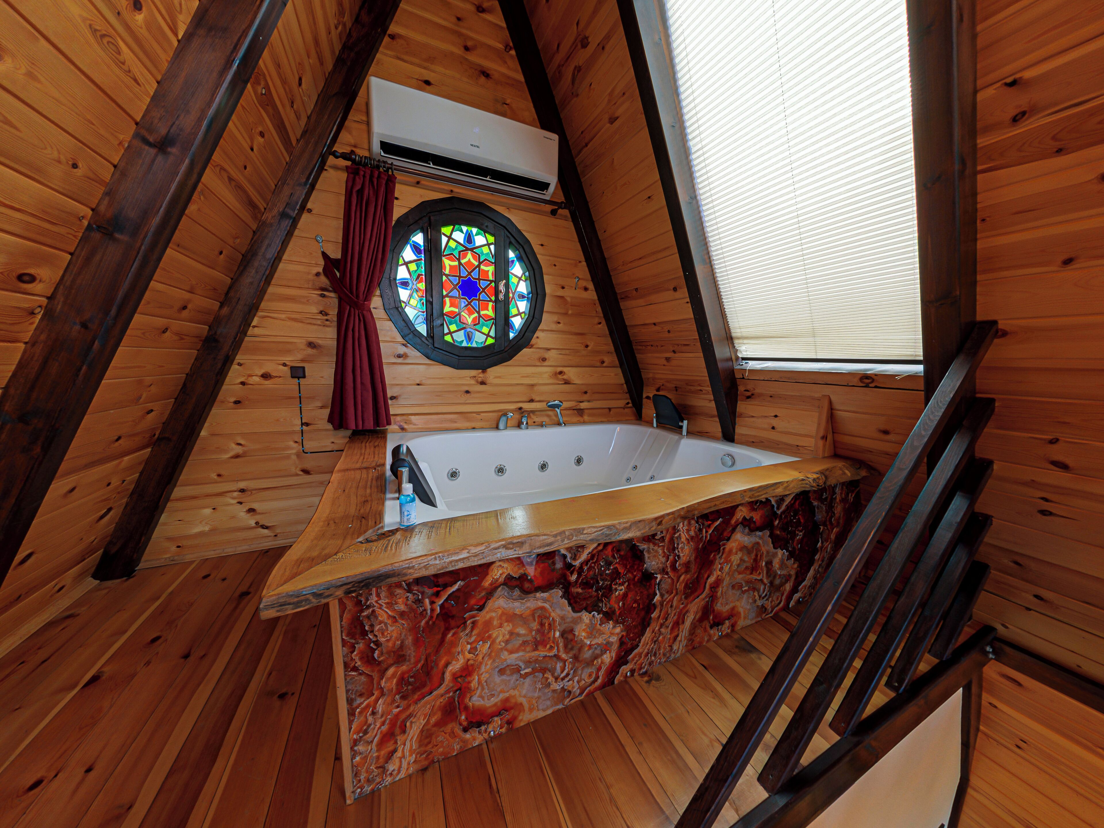 Un interior de madera con techo inclinado, una bañera y una ventana de vitral.