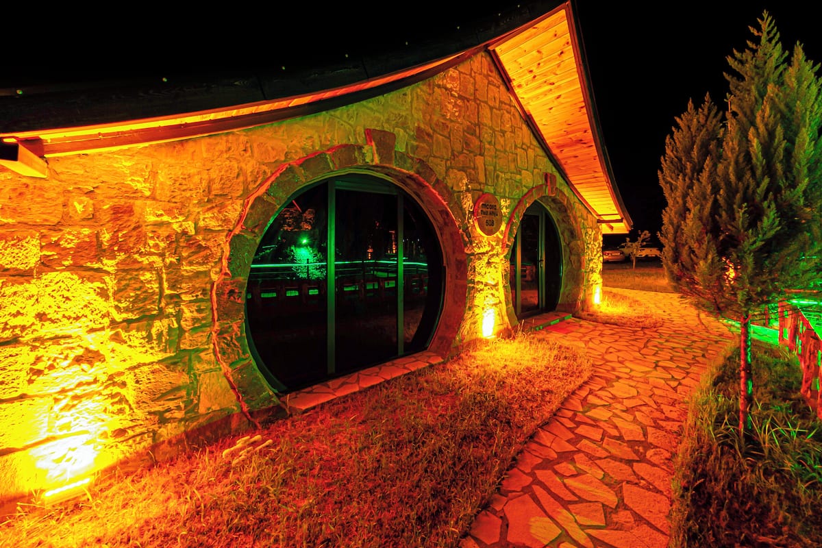 A building with stone walls and large arched windows, illuminated by warm lighting.