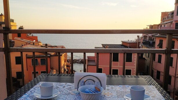 Een balkon met een tafel voor twee, uitkijkend op een kustgezicht.