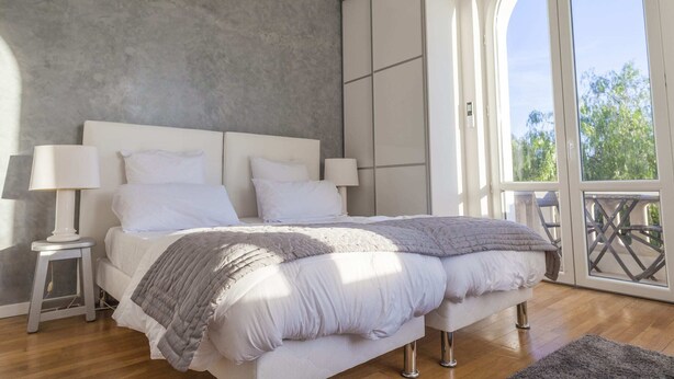 Une chambre avec un grand lit, deux lampes de chevet, une couverture grise à texture et une vue sur la verdure grâce à une porte-fenêtre coulissante.