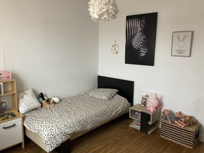 Un dormitorio con cama, mesita de noche, cómoda, estante con juguetes y decoración en la pared.