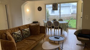 A cozy living room with a brown sofa, a small round table, and a dining area with a table and chairs. - Townhome (Lanester)