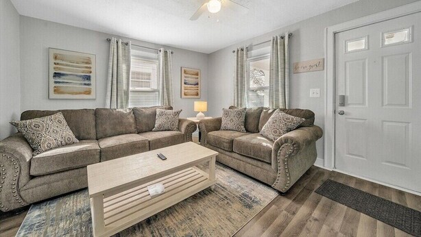 A living room with two sofas, a coffee table, a ceiling fan, and a door.