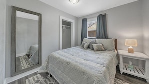 A bedroom with a large bed, a nightstand, a mirror, and a window with curtains.