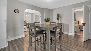 A dining area with a wooden table and chairs, a clock on the wall, and a plant on the table.