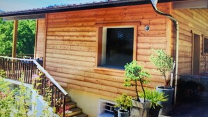 A wooden cabin with a balcony, potted plants, and a window. - 3 Bedroom Villa in Dingy-Saint-Clair (Dingy-Saint-Clair)