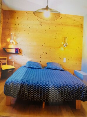 A room with a wooden wall, a bed with blue bedding, a chair, and a hanging light fixture. - 3 Bedroom Villa in Dingy-Saint-Clair (Dingy-Saint-Clair)