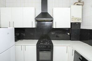 Una cocina con armarios blancos, una estufa negra y un lavavajillas blanco.