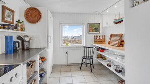 Una cocina compacta con muebles blancos, una silla negra y una ventana con vistas a edificios.