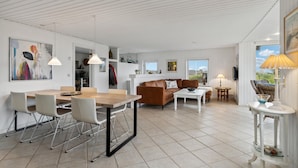 Amplia sala de estar con mesa de comedor, sillas, sofá y una mesita de centro. Hay lámparas colgantes, una lámpara y vistas al exterior.