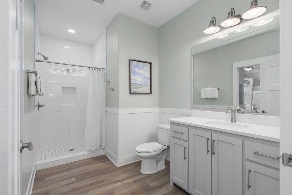 A modern bathroom with a shower, toilet, vanity, and a large mirror.
