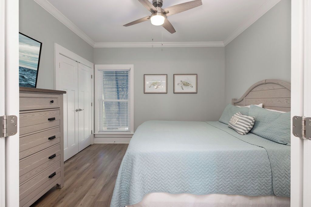 A bedroom with a bed, a ceiling fan, a dresser, and a window with blinds.