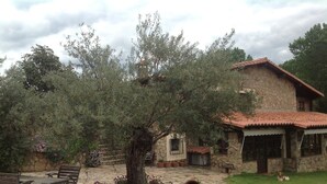 A stone house with a tiled roof, a paved patio with benches, and a lawn. - Finca vergel ****.HABITACIONES. bed and breakfast.  SIERRA DE GATA (sierra de gata)