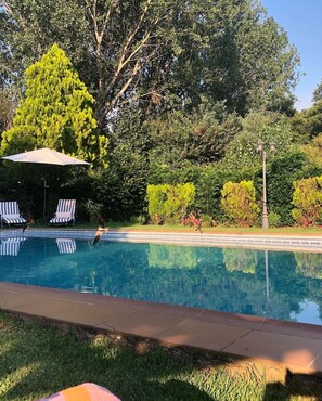 A swimming pool with lounge chairs and an umbrella, surrounded by lush greenery and a lamp post. - Finca vergel ****.HABITACIONES. bed and breakfast.  SIERRA DE GATA (sierra de gata)