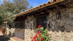 A stone building with a tiled roof, a wooden door, and a small porch area with potted plants. - Finca vergel ****.HABITACIONES. bed and breakfast.  SIERRA DE GATA (sierra de gata)
