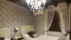 A bedroom with two beds, floral wallpaper, a chandelier, an air conditioning unit, and a wooden wardrobe. - Finca vergel ****.HABITACIONES. bed and breakfast.  SIERRA DE GATA (sierra de gata)