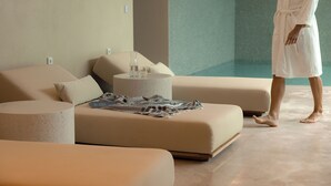 A modern spa room with a large bathtub, a seating area with a patterned throw, and a person in a bathrobe.